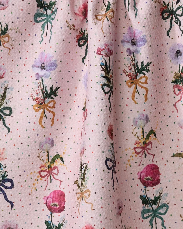 A close-up of the Pascale Dilger "Bows and Dots" tea towel, ultra-absorbent in light pink with polka dots and vertical rows of watercolor-style flowers tied with green, yellow, and red bows.