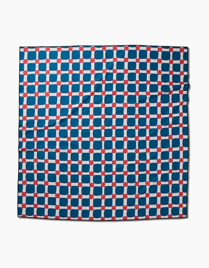 The Box Check Picnic scarf by Hufton Studio features a grid of blue squares and red dots on white. Made from quick-drying recycled fabric, it has a smooth, slightly wrinkled finish.