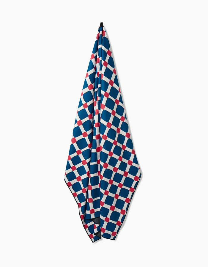 The Box Check Picnic towel by Hufton Studio hangs vertically and dries quickly, showcasing a geometric grid of blue, white, and red squares and circles on a crisp white background.