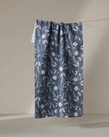 The Boyce Blue kitchen towel by Becki Owens features a blue and white floral pattern with subtle pink accents, hanging from a thin string against a plain, light-colored background.