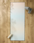 The GEOMETRY Breathe yoga mat lies on a wooden floor, with a water bottle at one end and a non-slip towel draped beside two grey yoga blocks at the other.