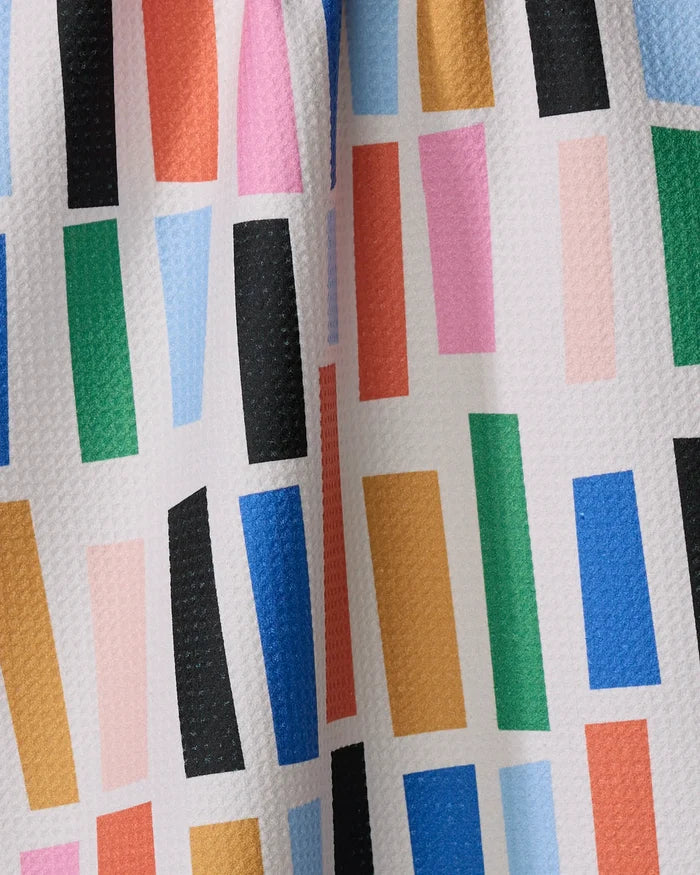 The Bricks tea towel by Jennifer Bouron features vibrant, randomly arranged blue, green, pink, red, orange, and black rectangles on a textured white background, and is crafted from recycled materials.