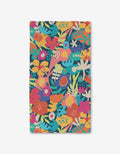 The Sareka Unique Bright Bunch bath towel is rectangular and ultra-absorbent, made from recycled materials with a vibrant floral print in red, orange, yellow, pink, teal, and green on a dark background.