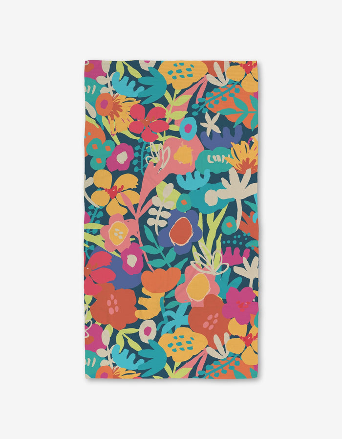 The Sareka Unique Bright Bunch bath towel is rectangular and ultra-absorbent, made from recycled materials with a vibrant floral print in red, orange, yellow, pink, teal, and green on a dark background.