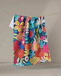 The Sareka Unique "Bright Bunch" tea towel, featuring a bold floral pattern in red, yellow, blue, and green, hangs from a clothesline against a neutral background. Its colorful design and quick-drying fabric make it both stylish and practical.