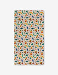 A rectangular cloth from Genna Blackburn called Bugs, made with eco-friendly towels, features a playful pattern of bugs in green, yellow, red, and blue with volcanoes, trees, and scattered leaves on a white background.
