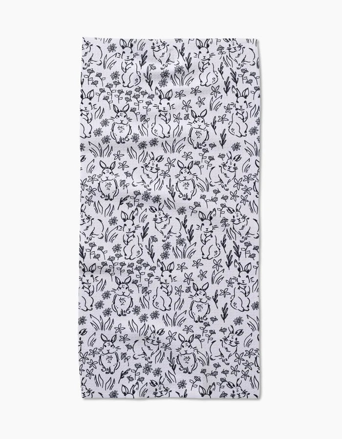 The Bunny Rabbit Garden by Charlie Rowan Designs is a white rectangular fabric with a close black line art pattern of rabbits, flowers, and leaves—ideal as a quick-drying towel for your kitchen or bar.
