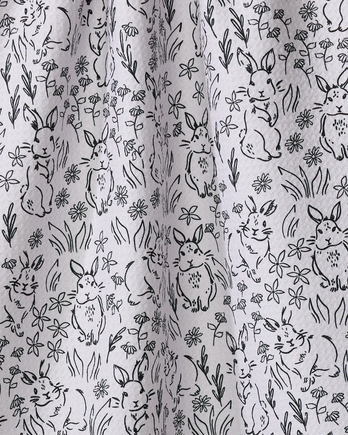 The Bunny Rabbit Garden tea towel from Charlie Rowan Designs features black line drawings of rabbits and flowers on light gray recycled fabric, combining eco-friendly materials with a charming, stylish design for your kitchen.