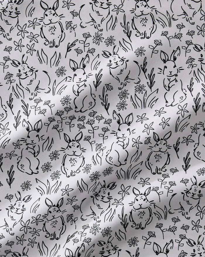 The Bunny Rabbit Garden dinner napkin set by Charlie Rowan Designs features black and white Geosuede fabric with hand-drawn bunnies in playful poses amid flowers and grass, adding a whimsical touch to your table.