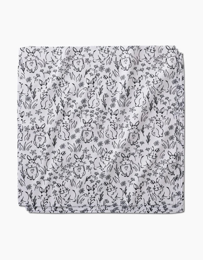 The “Bunny Rabbit Garden” Dinner Napkin Set by Charlie Rowan Designs features white fabric with a black line-art pattern of playful bunnies, flowers, and plants—an eco-friendly way to add whimsical charm to any table setting.