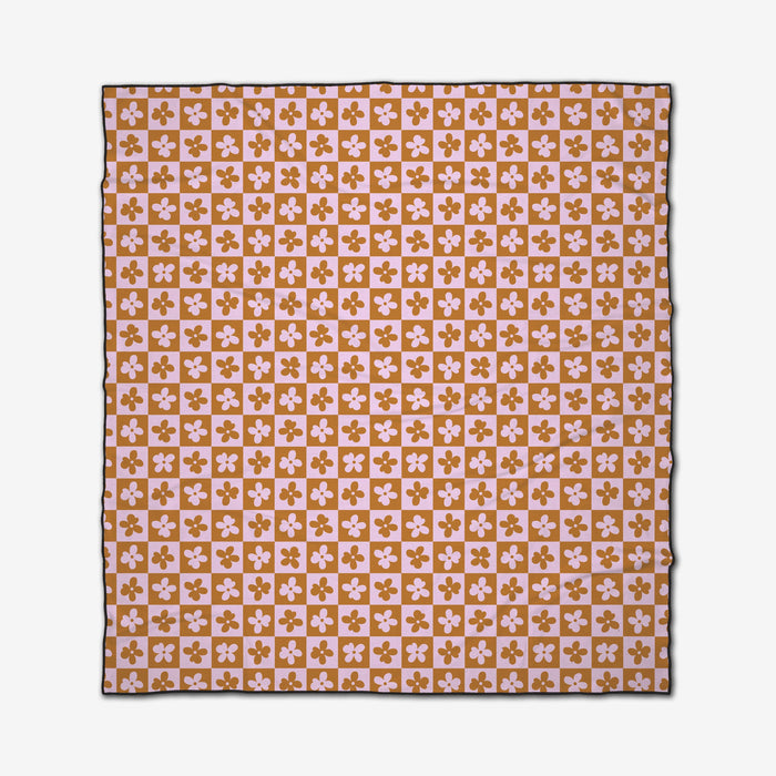 The Burnt Orange Flowers beach blanket by GEOMETRY features a square design with quick-dry fabric and a repeating pink and mustard checkerboard pattern adorned with four-petal florals, finished with a slim dark border.