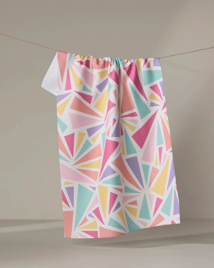 The "Burst" tea towel by Rebecca Bobko features a pastel geometric triangle pattern and hangs against a neutral backdrop. Made from recycled materials, this ultra-absorbent towel adds a bright touch to any kitchen.