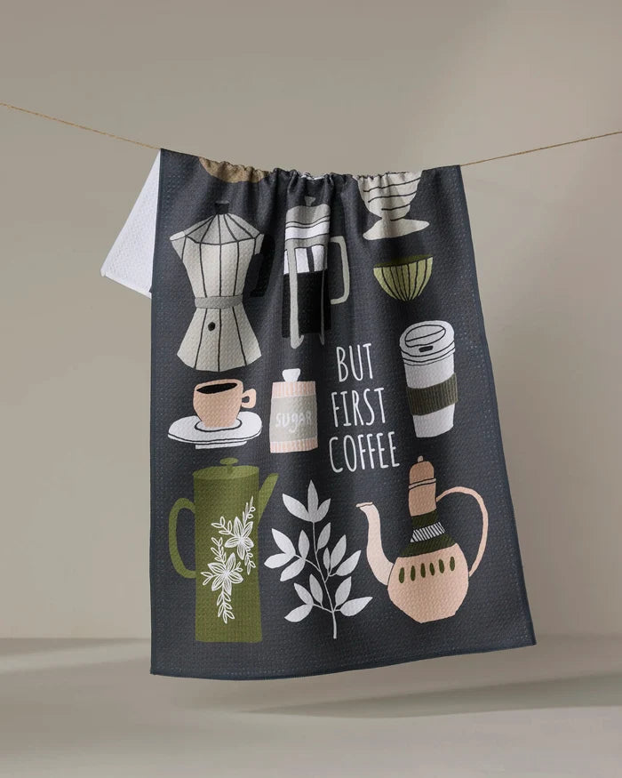 The "But First, Coffee" tea towel by Cottonflower Studio is made from recycled materials and features illustrations of coffee cups, a coffee pot, a sugar jar, and a French press, with the phrase “But First Coffee” displayed as it hangs.