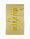 The GEOMETRY Butter yellow tea towel is made from Geoweave fabric, printed vertically with BUTTER in bold yellow letters and featuring a subtle textured pattern, shown laid flat on a white background.
