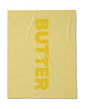 A yellow, silky-soft square cloth by Geometry, made from post-consumer recycled materials, features BUTTER in bold vertical letters down the right side.