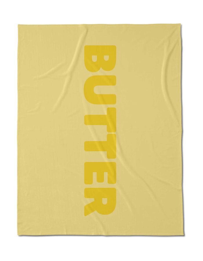 A yellow, silky-soft square cloth by Geometry, made from post-consumer recycled materials, features BUTTER in bold vertical letters down the right side.