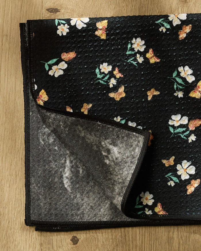 The "Butterfly Garden" Paw Towel by Danelys Sidron features a black textured surface with white flowers and yellow butterflies, plus a gray underside—an ultra-absorbent, stylish, and functional towel for your dog.