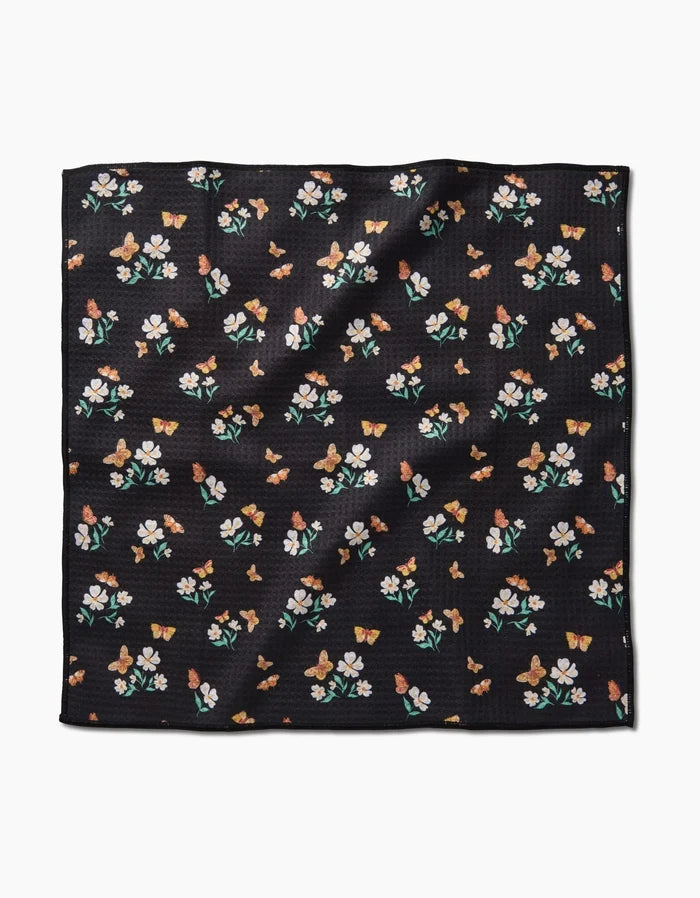 The Danelys Sidron Butterfly Garden is a square black Paw Towel made from ultra-absorbent Geoweave fabric, featuring a pattern of small colorful flowers and butterflies on its slightly textured surface.