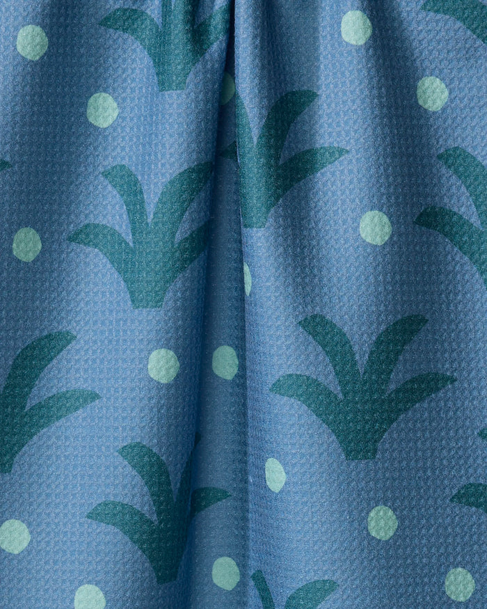 The Cactus Dot tea towel by Elizabeth Edwards features blue textured fabric with green abstract plant shapes and light green dots, crafted from recycled materials. A vertical fold runs down the center.