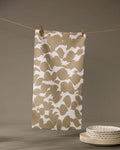 The Geometry Canopy bar towel, featuring a beige and white pattern and ultra-absorbent design, hangs from a string with clothespins. In the foreground, white ceramic plates are stacked neatly on a gray surface.