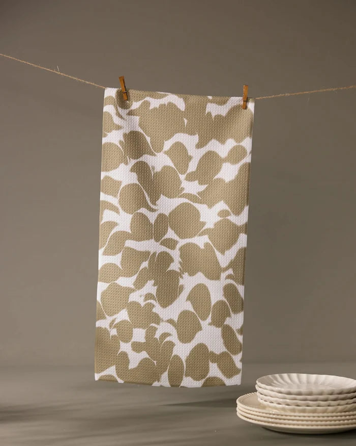 The Geometry Canopy bar towel, featuring a beige and white pattern and ultra-absorbent design, hangs from a string with clothespins. In the foreground, white ceramic plates are stacked neatly on a gray surface.