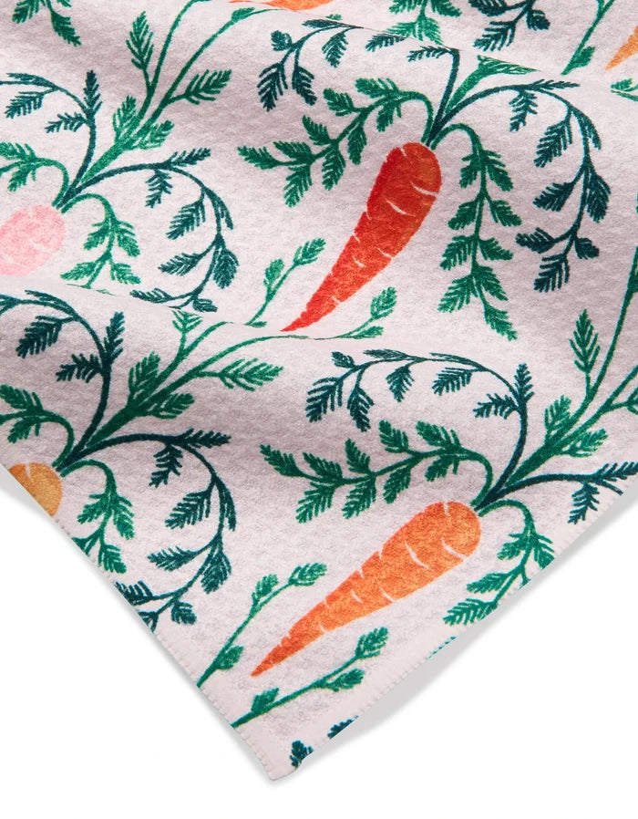 The Carrot Damask kitchen towel by Sarah Daugherty is white, recycled, and features a lively repeating print of orange carrots with green tops plus pink and yellow accents.