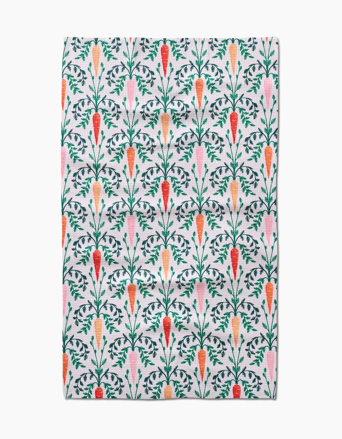 The Carrot Damask tea towel by Sarah Daugherty features a vertical carrot pattern in orange, red, and pink with green leaves on white. Made from absorbent recycled materials.
