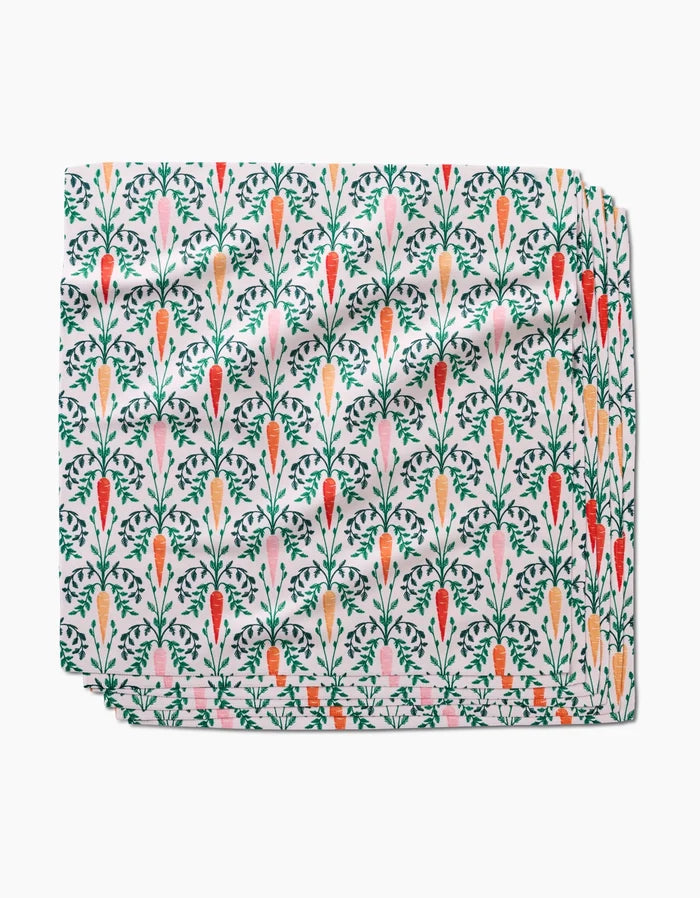 The Carrot Damask dinner napkin by Sarah Daugherty is an absorbent, neatly folded cloth featuring a vibrant pattern of colorful carrots and green leaves on a white background.