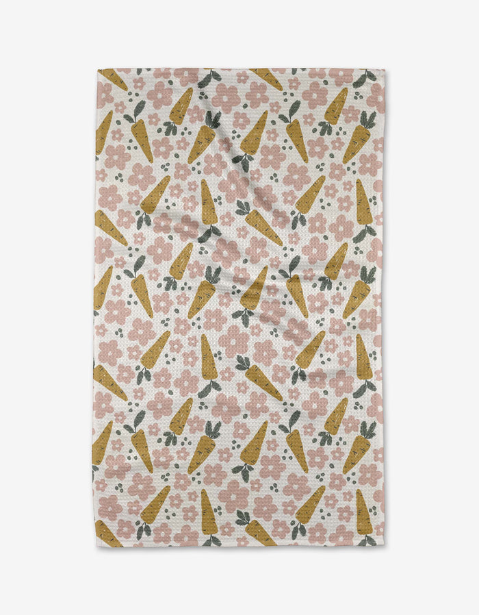 The Carrot Patch tea towel by Charlie Rowan Designs features a diagonal pattern of yellow carrots, pink flowers, and green leaves on white—a delightful kitchen accent.