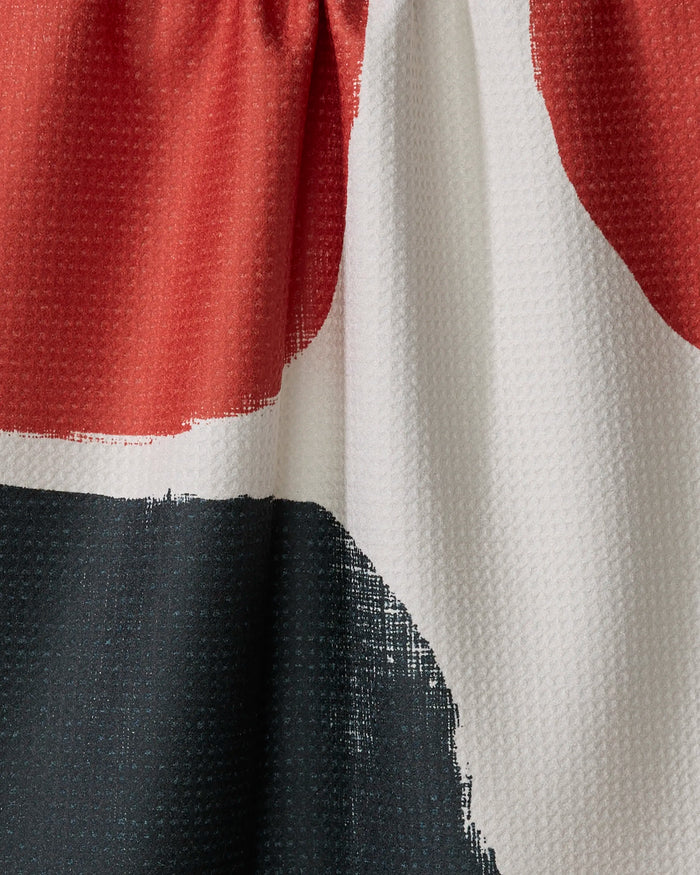 Close-up of Geometry's Cast tea towel, made from recycled materials, with visible weaves and gathered stitching at the top. Features bold, abstract color blocks in red, black, and white.