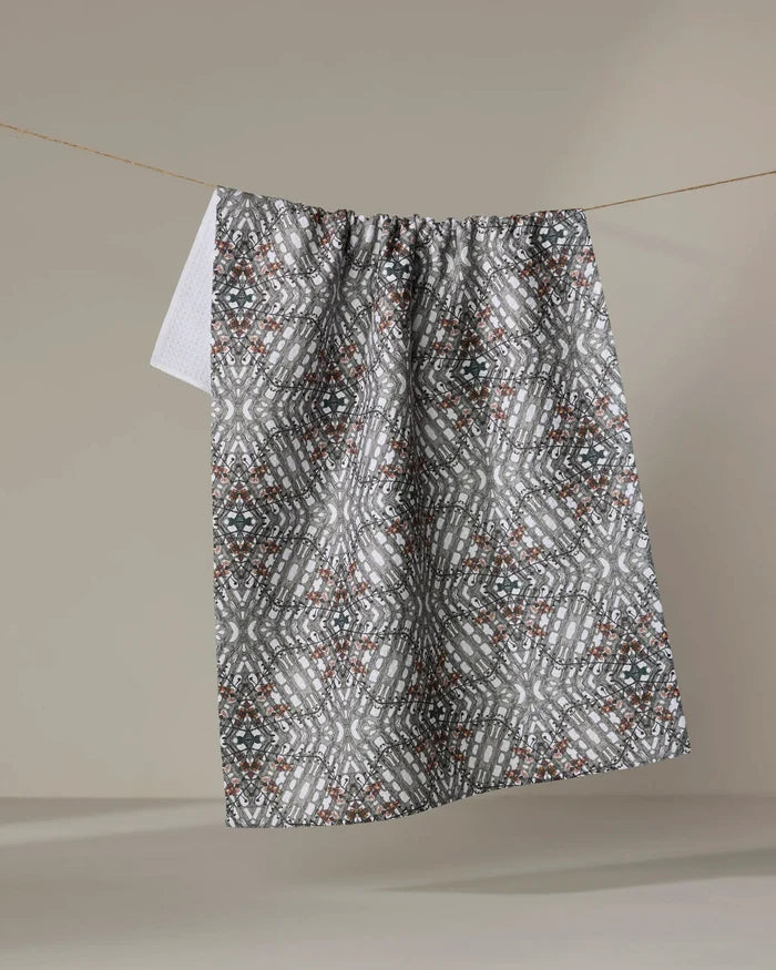 The Katherine Berkeley Cha Cha Interchange tea towel, featuring a quick-drying geometric design in gray, white, and brown, hangs on a clothesline against a plain beige background.