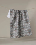 The Katherine Berkeley Cha Cha Interchange tea towel, featuring a quick-drying geometric design in gray, white, and brown, hangs on a clothesline against a plain beige background.