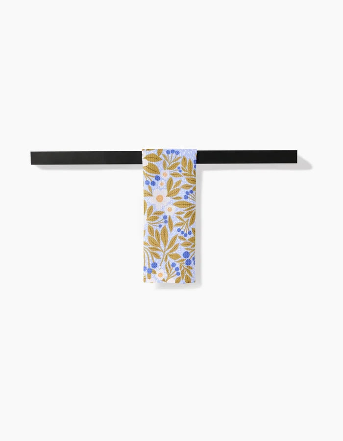 The Chamomile And Blue bar towel by Lisa Nelson, made from Geoweave fabric, displays yellow leaves and blue and white flowers, shown draped over a black bar on a white background.