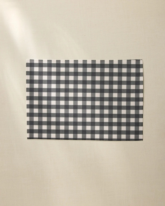 A Geometry Charcoal Gingham rectangular placemat is placed on a light beige textured surface.