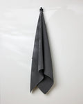 A GEOMETRY Charcoal waffle bath towel hangs neatly on a black hook against a plain white wall.