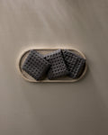 A wooden tray displays three GEOMETRY Charcoal waffle washcloths, neatly arranged on a light beige surface, with soft natural light creating gentle shadows.