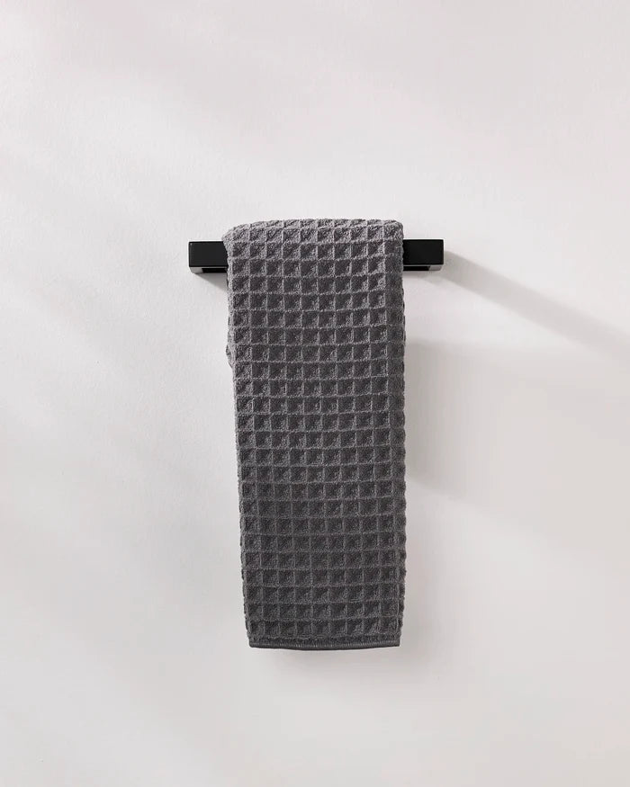A GEOMETRY Charcoal waffle hand towel hangs neatly on a black horizontal bar against a plain white wall.