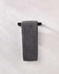 A GEOMETRY Charcoal waffle hand towel hangs neatly on a black horizontal bar against a plain white wall.