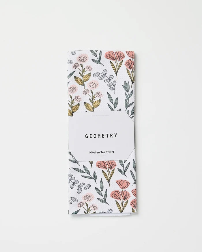 The Charolette Multi tea towel by Charlie Rowan Designs features ultra-absorbent fabric with a pink and yellow floral pattern, folded and wrapped in a white GEOMETRY Kitchen Tea Towel label, displayed on a plain white background.