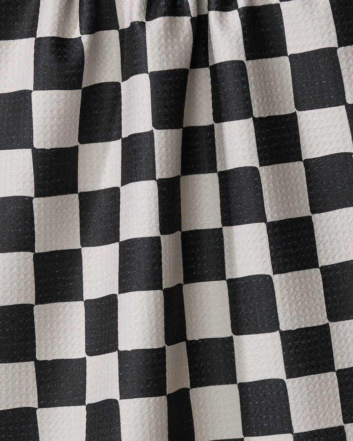 Close-up of Danelys Sidron’s Checkmate kitchen towel, featuring a black and white checkered pattern, textured surface, and gentle folds. Made from recycled materials, the fabric is arranged with gathered pleats at the top.