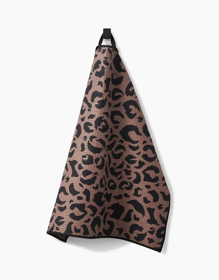 A Cheetah Hound Paw Towel by Geometry, featuring a black leopard print on brown ultra-absorbent Geoweave™ fabric, hangs from a black loop against a white background.