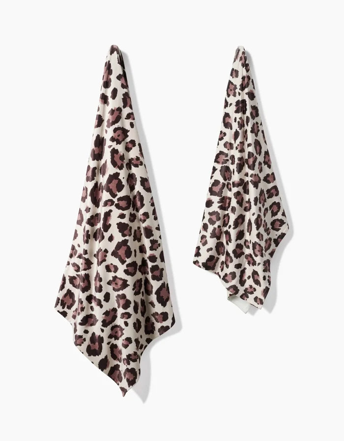 Two Cheetah towels by Geometry, featuring a brown and black leopard print and made from recycled materials, hang on a white wall—one large, one small.