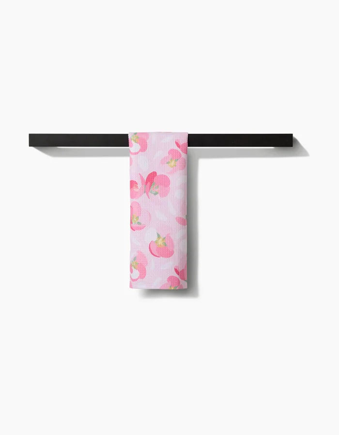 The Cherry Blossom Bar Towel by Rebecca Bobko, made from Geoweave fabric, displays red and pink floral patterns and hangs over a black towel rack against a white background.
