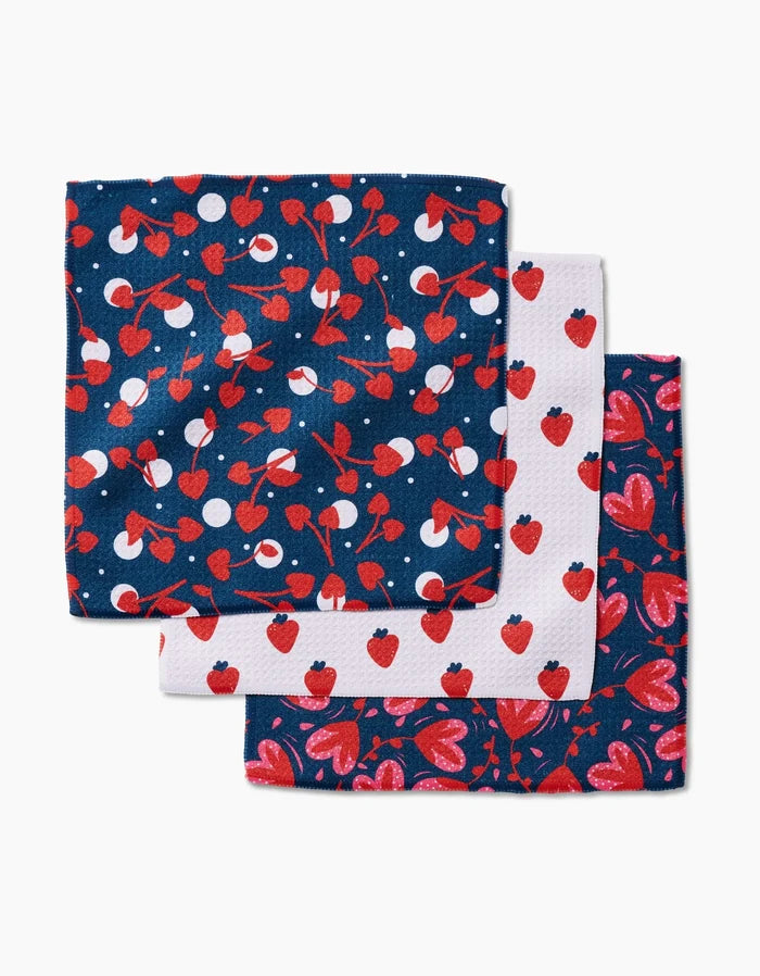 The Cherry Love kitchen towel set by Charlie Rowan Designs features three recycled towels: cherries and white dots on navy, strawberries on white, and strawberries with hearts on dark blue.