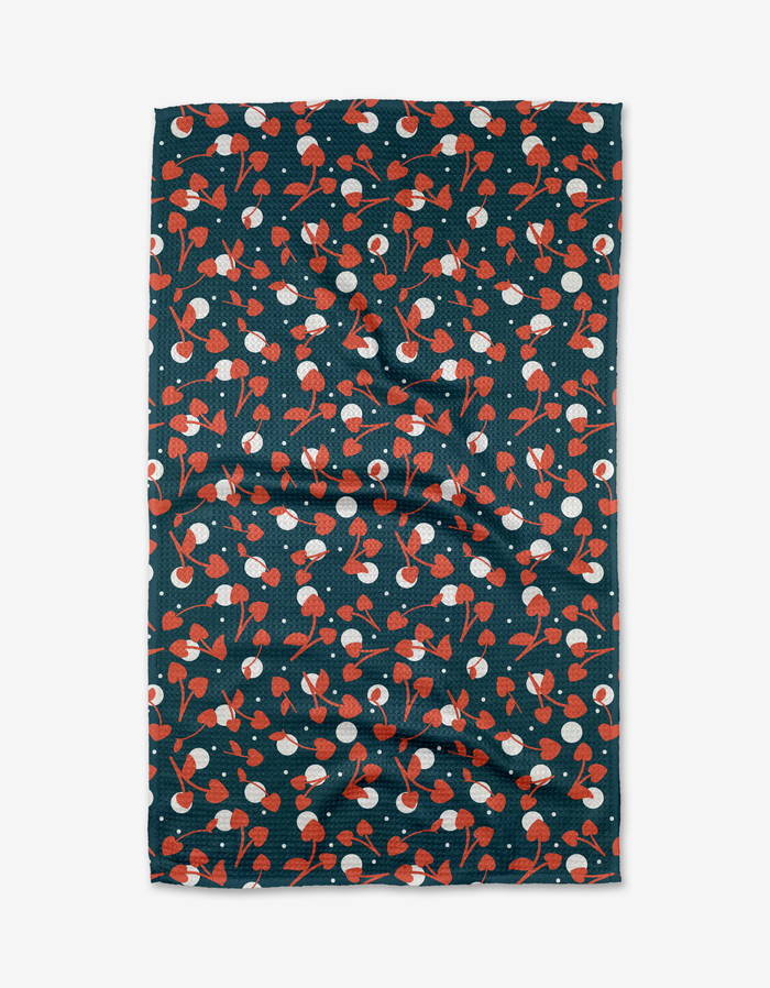 The Cherry Love tea towel by Charlie Rowan Designs features a playful pattern of red and white cherries with green stems on a dark Geoweave fabric background, arranged randomly across its rectangular surface.