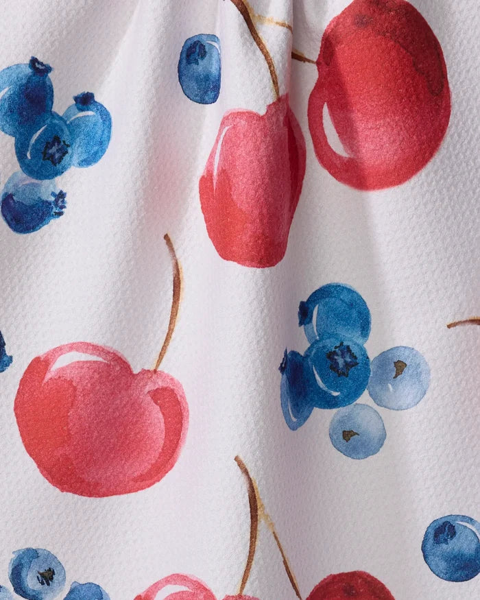 Close-up of Elena Fay’s "Cherry On Top" tea towel, showcasing a white textured fabric with a vibrant watercolor pattern of red cherries and blue blueberries.