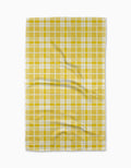 The GEOMETRY Churned tea towel, made from Geoweave fabric and showcasing a yellow and white plaid design, lies flat with gentle creases on a plain white background.