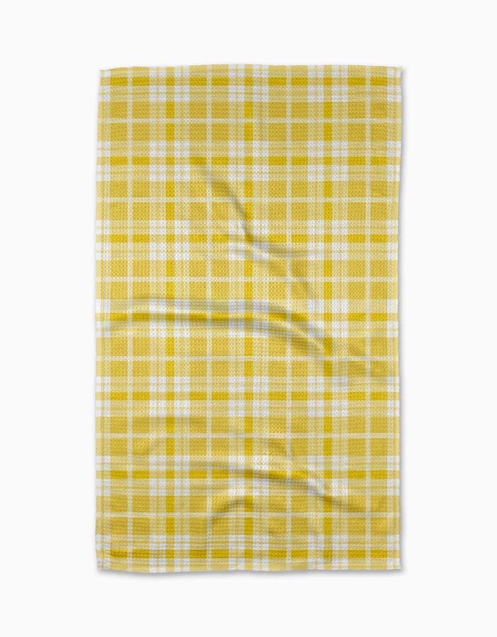 The GEOMETRY Churned tea towel, made from Geoweave fabric and showcasing a yellow and white plaid design, lies flat with gentle creases on a plain white background.