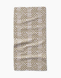 The Studio Jeannot Chutes Avocado is a rectangular bar towel made from Geoweave fabric, featuring a geometric pattern of brown and white rectangles with horizontal white lines on a neutral background. It is shown slightly wrinkled on a white surface.