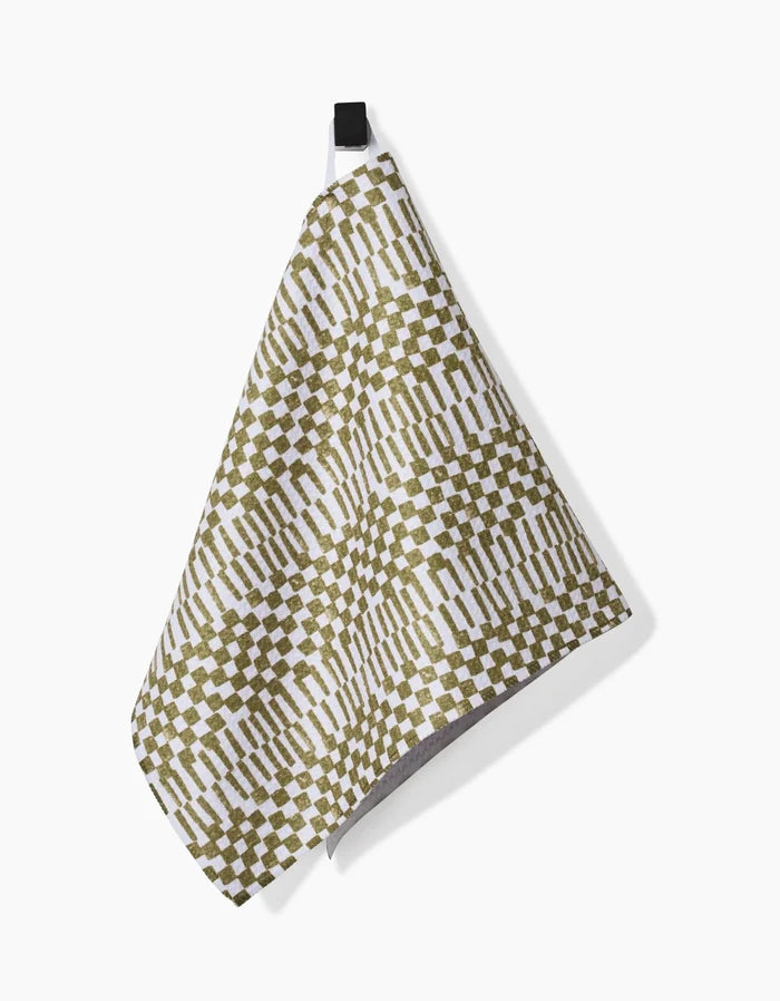 The Studio Jeannot Chutes Avocado Bar Towel features a green and white checkerboard and stripe design on Geoweave fabric, hanging from a black loop against a white background.